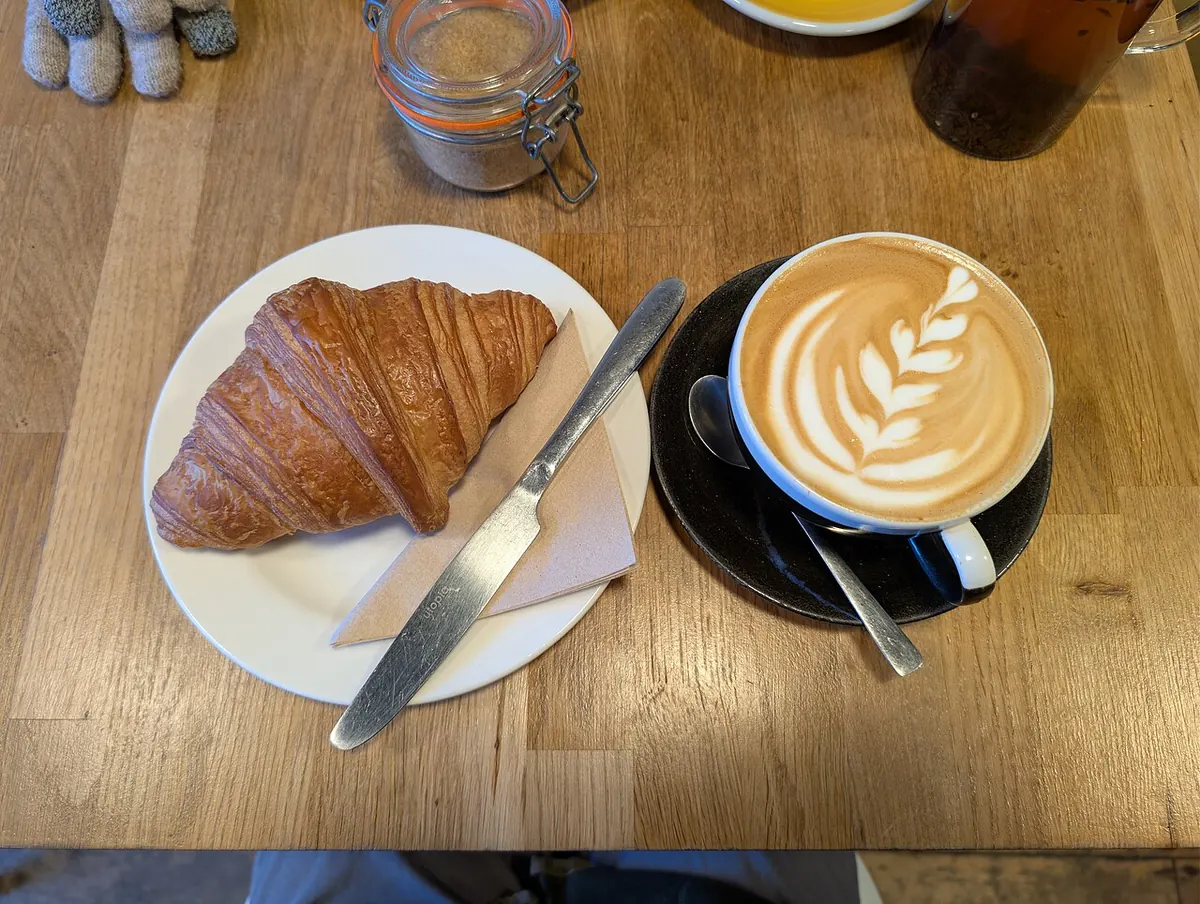 Croissant con un capuchino sobre una mesa de madera